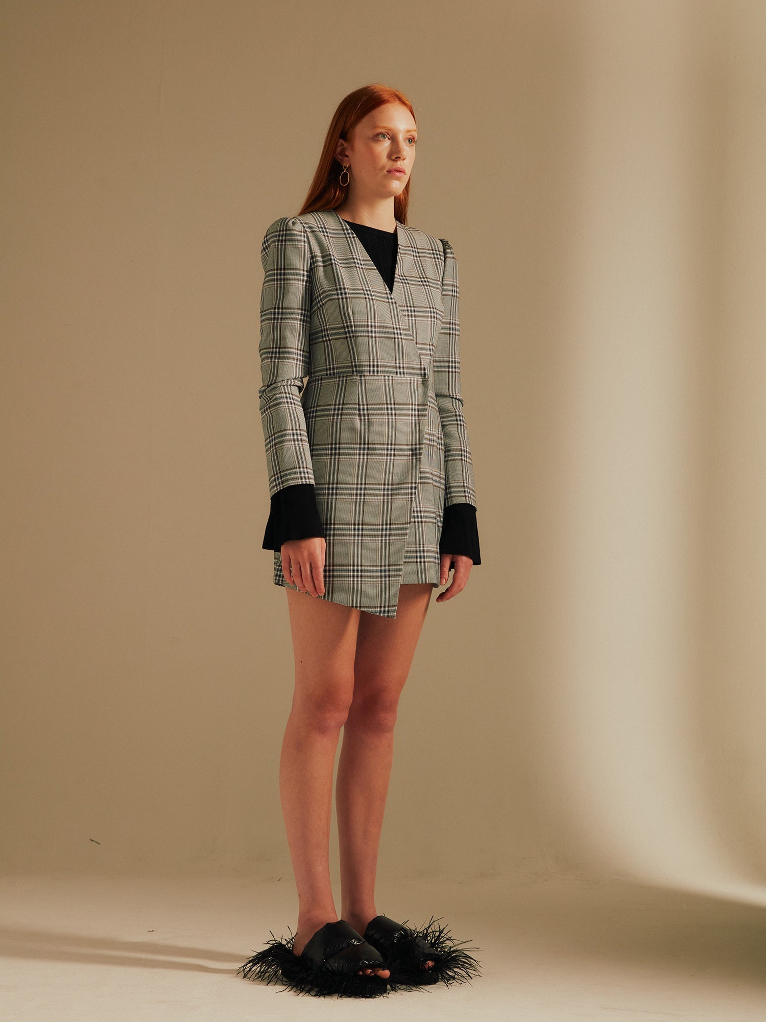 model faces sideways standing straight in the Amelia Heritage Asymmetric Blazer Dress with fluffy slippers