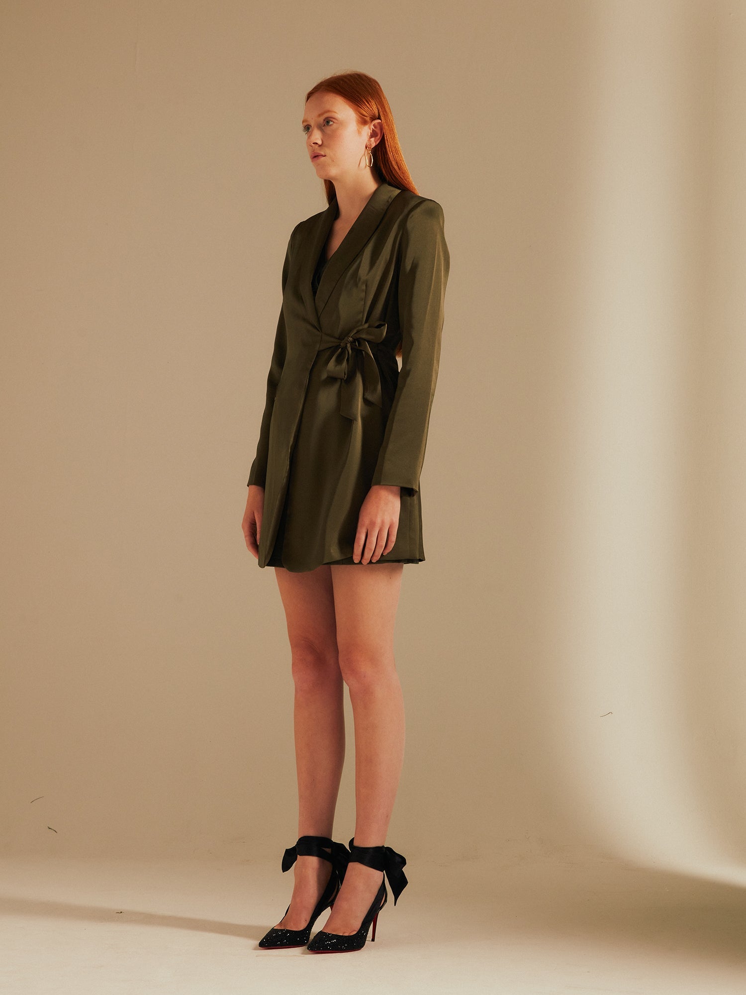 model faces the side wearing the Alexandria Tie-side Blazer Dress with black heels in a studio