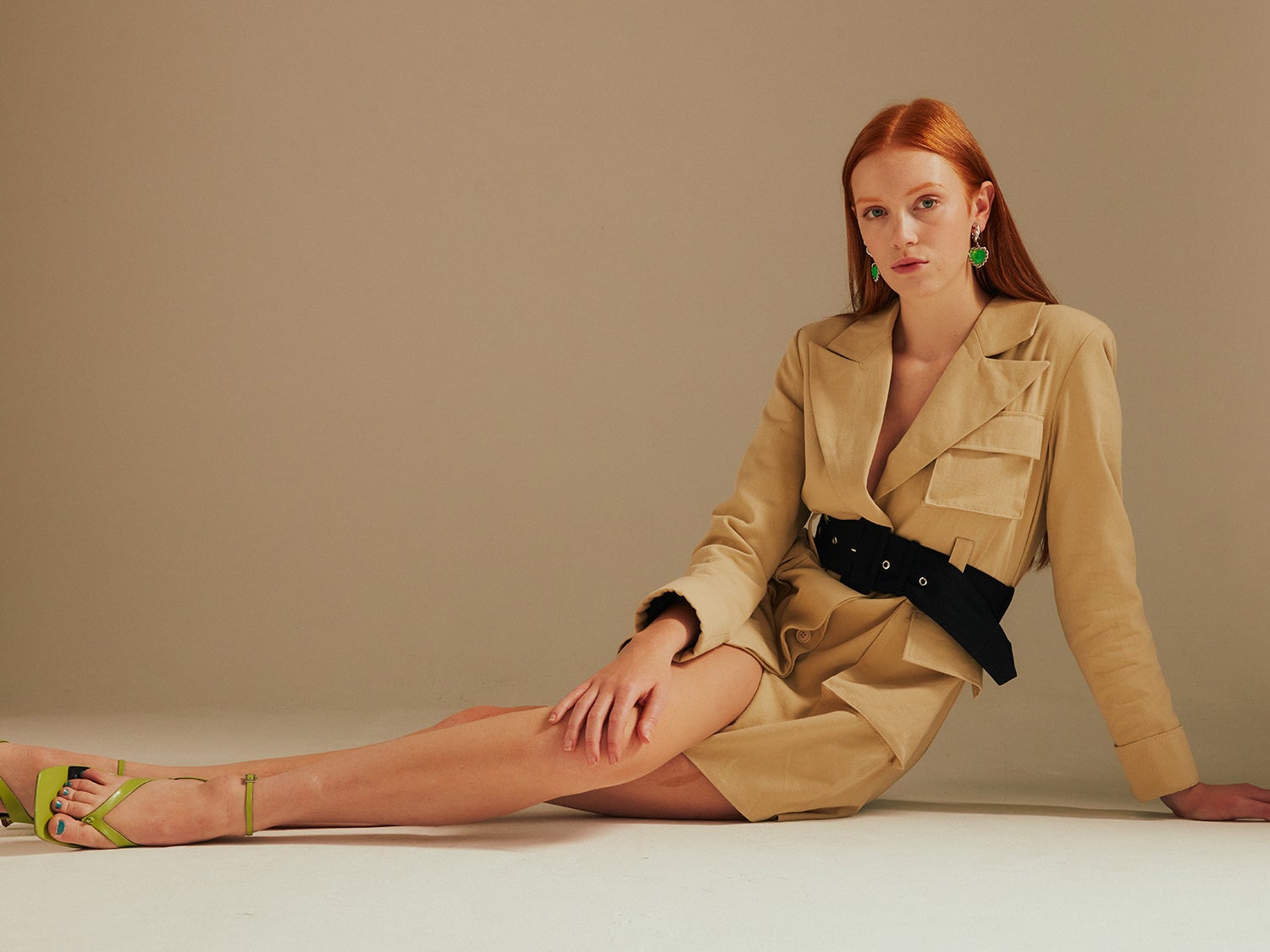 a landscape image of the model with her hand on her knee lying on the floor in the Ashley Utility Belted Blazer Dress